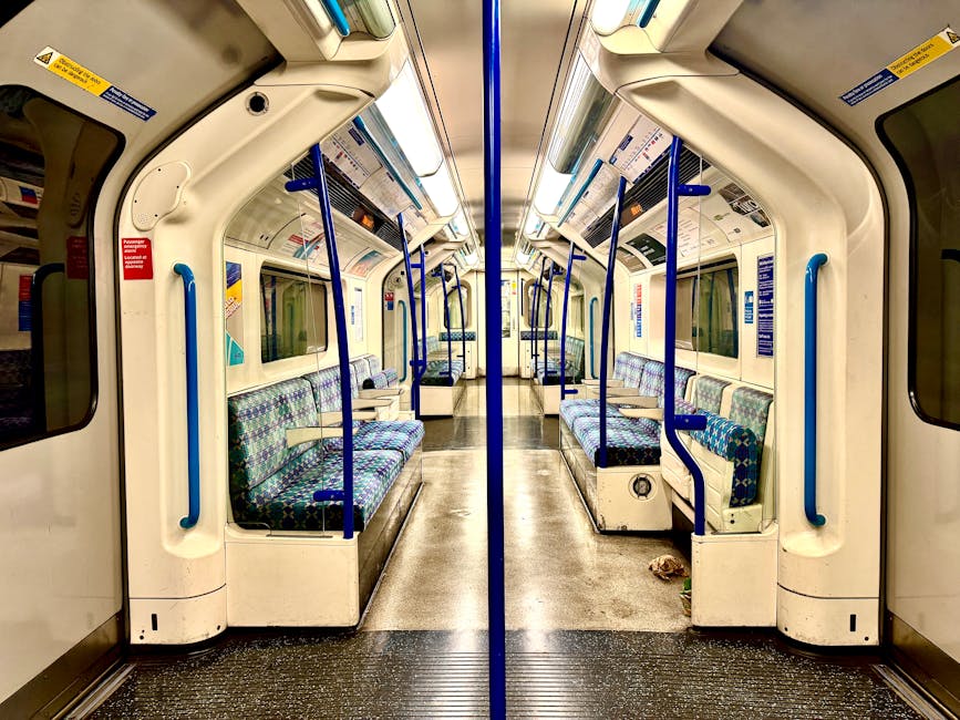 Inside an underground London tube station, the platform features white tiled walls with red and green accents, displaying the station name 'Archway'. Several passengers are waiting, some standing near